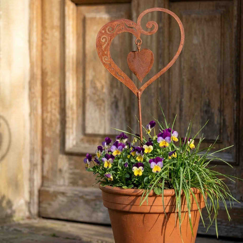 Edelrost Herz mit beweglichem Innenherz als Gartenstecker im Terracotta-Topf mit Hornveilchen vor rustikaler Holztür - handgefertigt in Bayern von Rostikal